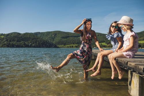 three women sitting on a dock in the water at Ferienwohnung mit Garten in ruhiger Lage am Waldrand in Pöllauberg
