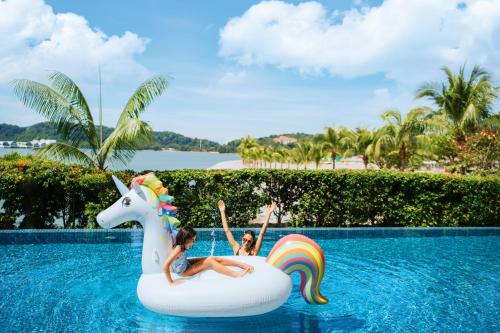 two children riding on an inflatable unicorn in a swimming pool at Lexis Hibiscus Port Dickson in Port Dickson