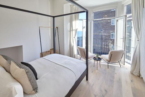 a bedroom with a bed and two chairs and windows at Pier View in Saltburn-by-the-Sea