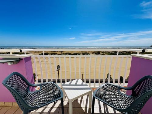 two chairs and a table on a balcony with the beach at Hotel Lux in Caorle