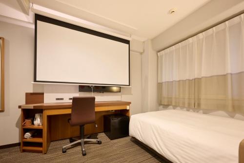 a bedroom with a bed and a desk with a projector screen at Via Inn Shin Osaka in Osaka