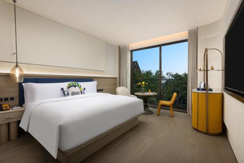 a bedroom with a white bed and a large window at voco Xishuangbanna Gaozhuang by IHG in Jinghong