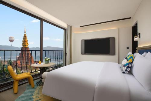 a bedroom with a bed and a balcony with a view at voco Xishuangbanna Gaozhuang by IHG in Jinghong