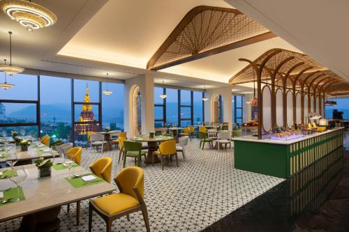 a restaurant with tables and chairs and windows at voco Xishuangbanna Gaozhuang by IHG in Jinghong