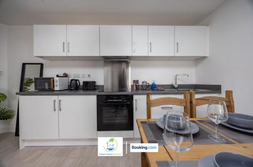 a kitchen with white cabinets and a table with wine glasses at Cosy Retreat By Green Haven Escapes Short Lets & Serviced Accommodation Seacroft With Free Off-Street Parking & Pet-Friendly in Killingbeck