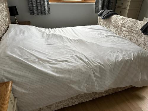 a bed with a white sheet on top of it at Honeybee Cottage in Lincolnshire
