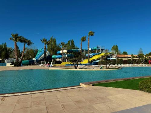 une piscine avec un toboggan dans un parc avec des palmiers dans l'établissement Mobil-home Elite 4-6 pers - Vias Camping La Carabasse, à Vias