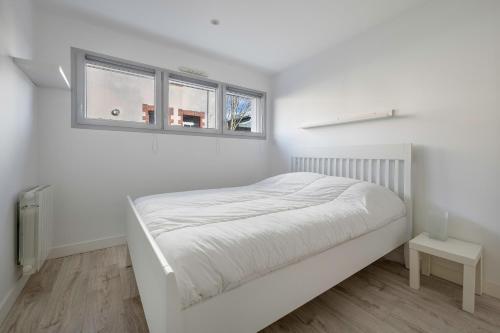 ein weißes Schlafzimmer mit einem Bett und zwei Fenstern in der Unterkunft Appart dans bourg a 230m de la plage - 4 pers in La Bernerie-en-Retz