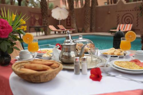 a table with breakfast food and a swimming pool at Fibule Du Draa Kasbah D'hôtes in Zagora