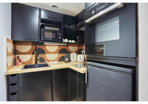 La cuisine est équipée de placards noirs, d'un évier et d'un lave-vaisselle. dans l'établissement Apartment Le Marais Place des Vosges by Studio Prestige, à Paris