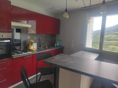 une cuisine avec des placards rouges et un comptoir avec des chaises dans l'établissement Cocon au milieu des montagnes, à Saint-André-dʼEmbrun