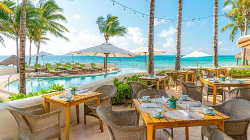 an outdoor restaurant with tables and chairs and the ocean at Mahekal Beach Front Resort & Spa in Playa del Carmen