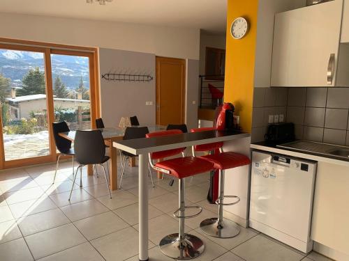 une cuisine avec une table, des chaises rouges et un comptoir dans l'établissement Villa proche du plan d'eau, à Embrun