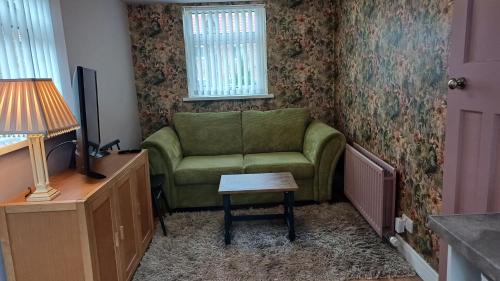 a living room with a green couch and a table at Garden Apartment Morpeth- with lockable bike storage! in Morpeth
