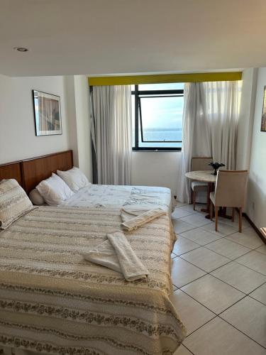 a bedroom with a bed and a table and a window at Flat Privativo Sol Victoria Marina in Salvador
