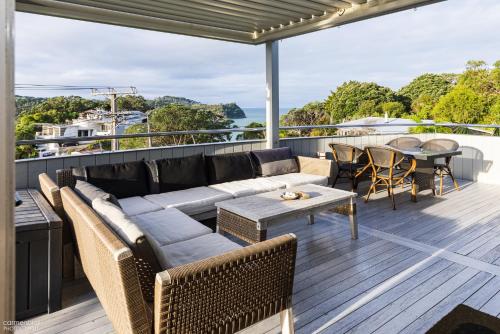 a patio with a couch and tables on a deck at Funky Beach House with sea and country views in Orewa