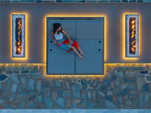 a woman sitting on a window in a room with lights at Anastasia Hotel & Suites Mediterranean Comfort in Karistos