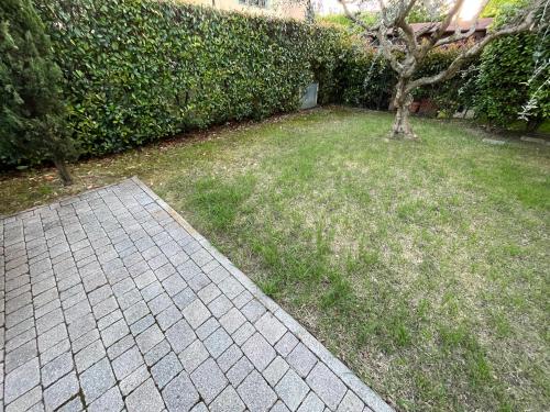a grassy yard with a tree and a brick sidewalk at Holiday House La Fornace in Pontedera