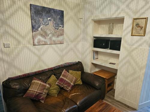 a living room with a brown leather couch with pillows at 3-Bed Cottage - fast WiFi-Big Garden - Town Centre in Kirriemuir