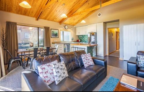 a living room with a leather couch and a kitchen at Ski Country Chalet in Ohakune