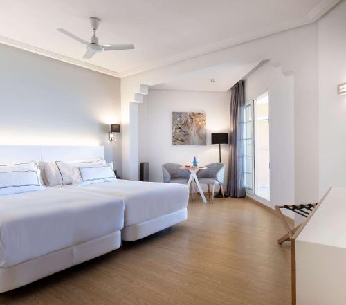 a white bedroom with two beds and a table at Meliá Isla Canela in Isla Canela