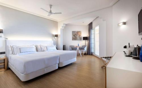 a white bedroom with a large bed and a table at Meliá Isla Canela in Isla Canela