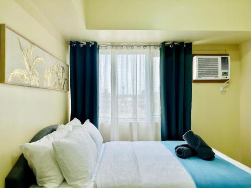 a bedroom with a bed with blue curtains and a window at 2F Cozy Studio Unit at Aspira Avida Tower 2 in Cagayan de Oro