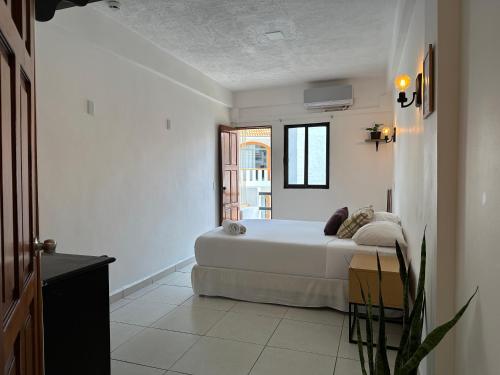 a white bedroom with a bed and a window at Calma Chicha Rooms in Playa del Carmen