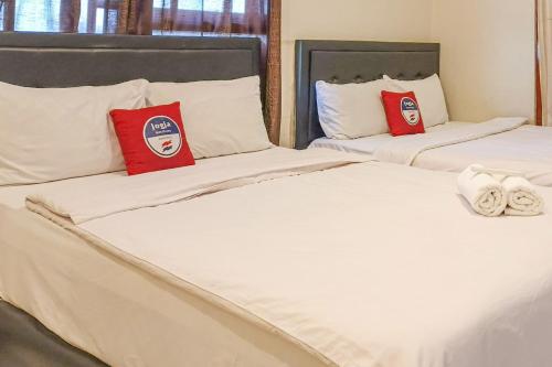 two white beds with red pillows in a room at D Martin Malioboro Hotel RedPartner in Sentool