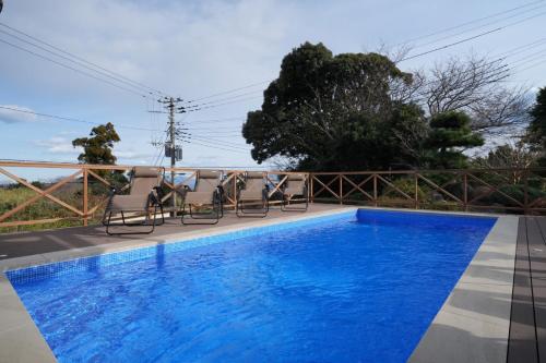 a blue swimming pool with chairs next to a house at パーパスリゾート EG Sky terrace 熱川 in Higashiizu