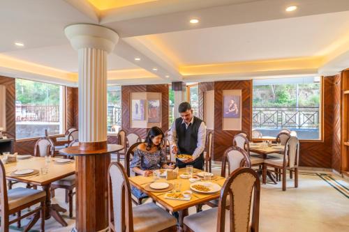 a man and woman sitting at a table in a restaurant at Karnika Resort Levelup Boutique-Dharamshala in Dharmsala