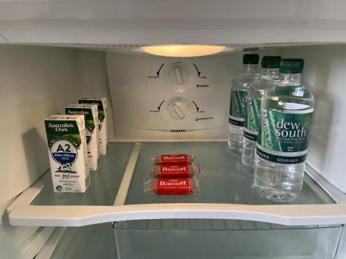 a refrigerator filled with bottles of water and milk at The Cozy Penguin with Sea Views in Cooee