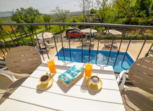 a table with two glasses and a book next to a pool at Vila sa bazenom Vrnjačka Idila in Vrnjačka Banja