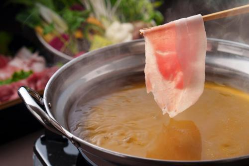 a piece of ham being dipped into a pot of food at GRANDVRIORESORT ISHIGAKIJIMA Ocean's Wing & Villa Garden in Ishigaki Island