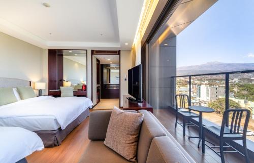 a bedroom with a bed and a couch and a balcony at Parksunshine Jeju in Seogwipo