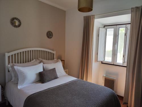 a bedroom with a bed with white pillows and a window at CASA NA ALDEIA in Estremoz