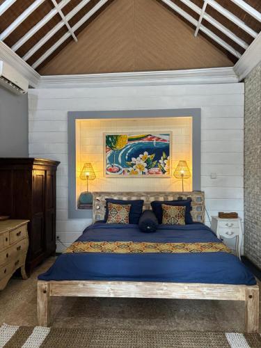a bedroom with a blue bed with a painting on the wall at villa Angin in Munggu