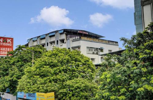 a tall white building with trees in front of it at Super Hotel O Golden Suites in Turambhe