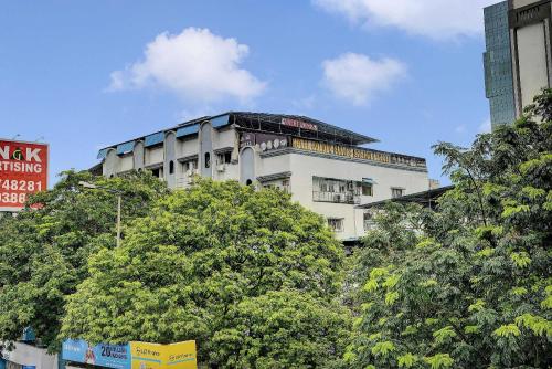 a tall white building with trees in front of it at Super Hotel O Golden Suites in Turambhe