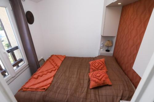 Ce lit se trouve dans une petite chambre dotée d'une couverture orange. dans l'établissement splendide et charme de la marina a St Cyp, à Saint-Cyprien