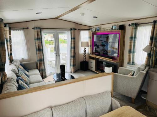 Una sala de estar con un sofá y un televisor. en Exquisite Lake lodge in Hoburne Holiday Resort - Valentino Rose Lodge, en South Cerney