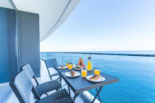 a table with food and drinks on a balcony with a pool at Mar Apartment by Atlantic Holiday in Câmara de Lobos