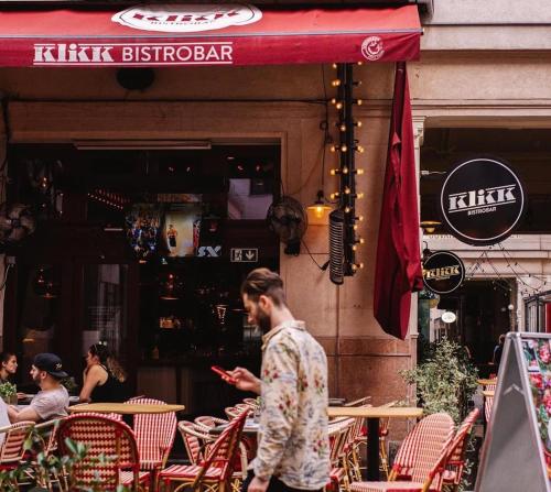 a man walking in front of a restaurant with his cell phone at Klikk Superior Apartments at Gozsdu in Budapest