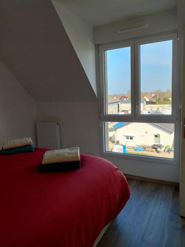 une chambre avec un lit rouge et une grande fenêtre dans l'établissement Appartement neuf, calme et ensoleillé, à Cabourg