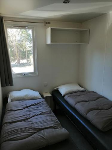 deux lits dans une petite pièce avec une fenêtre dans l'établissement bungalow au soleil camping les dunes, à Torreilles