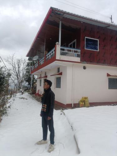 a man standing in the snow in front of a building at Kanatal vatika and home in Kanatal