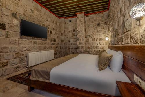 a bedroom with a bed and a tv on a stone wall at Latona Stone Palace in Nevsehir