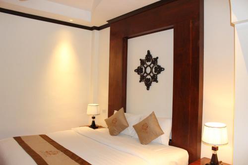 a bedroom with a bed with a wooden headboard and two lamps at Lux Hotel in Luang Prabang