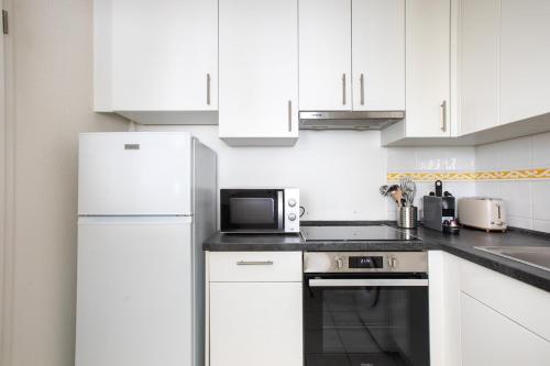 a white kitchen with white cabinets and a microwave at Appartement lumineux 3 frontières parking gratuit in Huningue