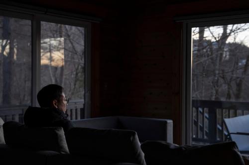 a man sitting on a couch looking out a window at Calm villa 富士山中湖 in Yamanakako